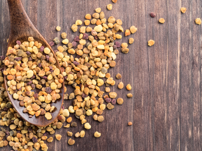 Closeup view of bee pollen in wooden spoon on brown wooden table. Copy space. Top view or flat lay.